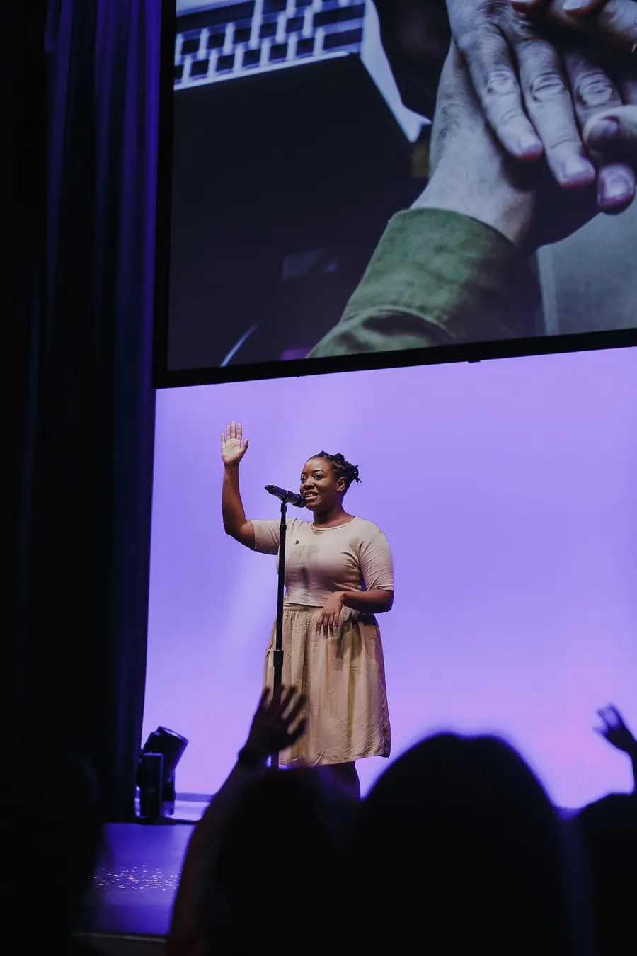 Asha on stage with one hand raised, a large screen behind her